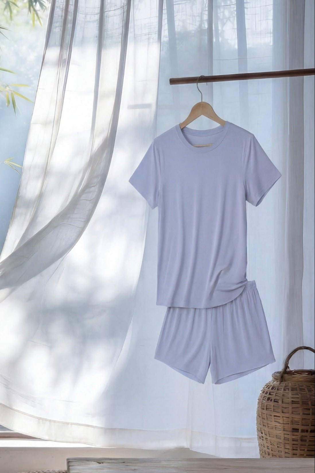 chambray blue relaxed tee and shorts set hanging on a hanger in front of a window with bamboo view