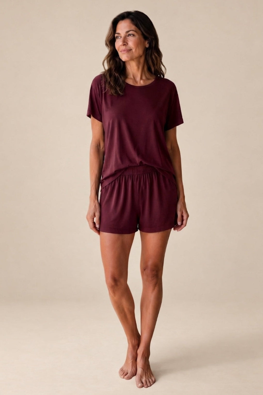 A woman modeling a matching bordeaux short-sleeve relaxed t-shirt and shorts set from Camofleur in a gorgeous bordeaux red against a solid beige studio background