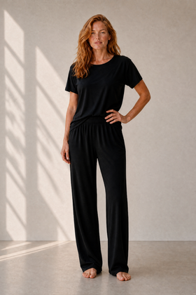 Woman wearing a black camofleur outfit standing in a well-lit room with sunlight casting shadows on the wall.
