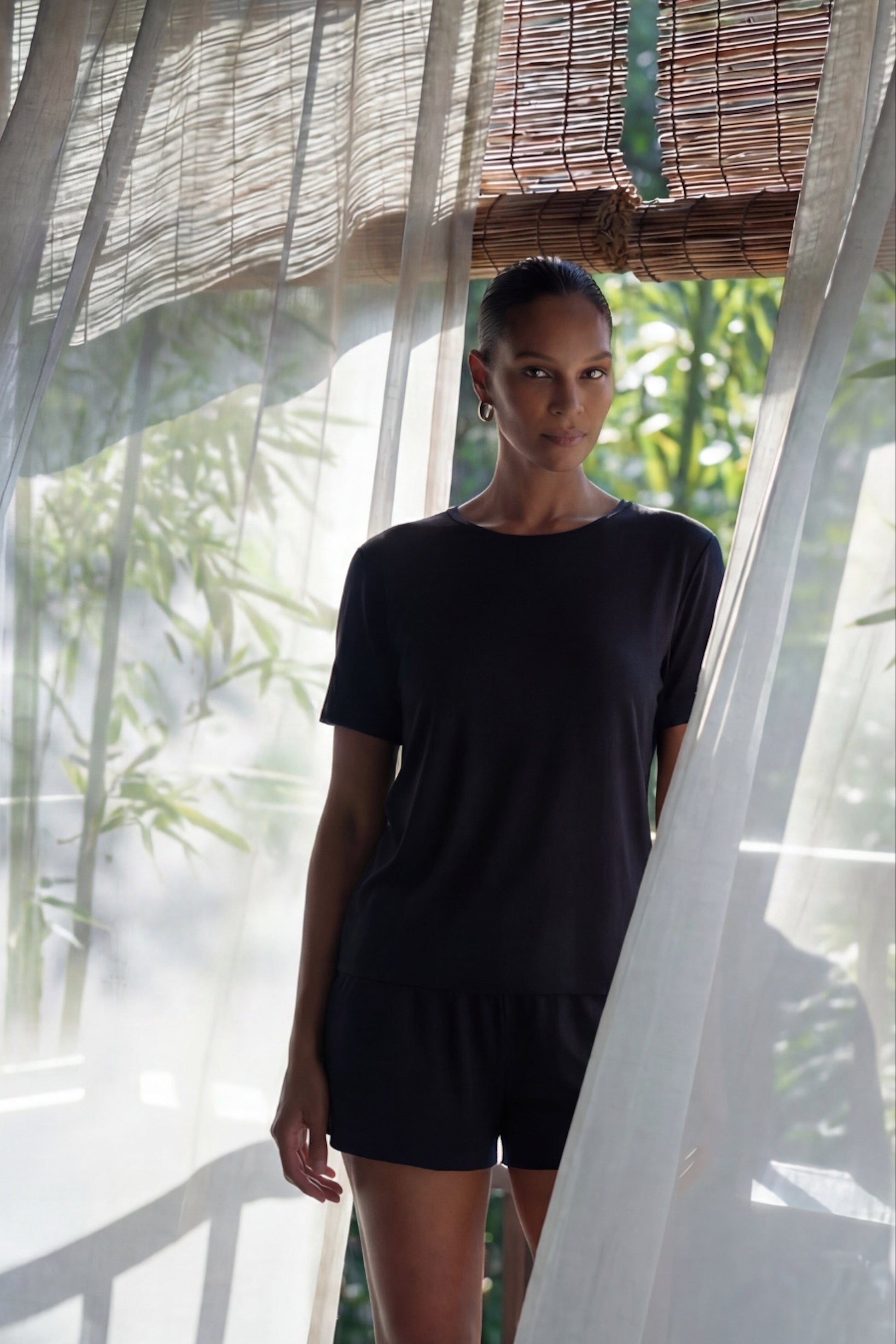 Woman wearing a black outfit standing behind sheer curtains with a natural background