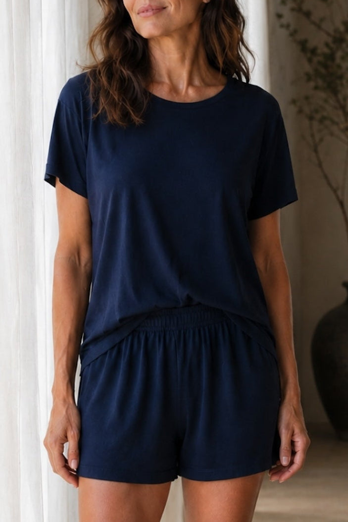 Woman wearing a navy blue outfit standing in a room with a vase and plant in the background.