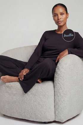 Person sitting on a gray chair wearing a noir black lounge set from camofleur with 'breathe' embroidery